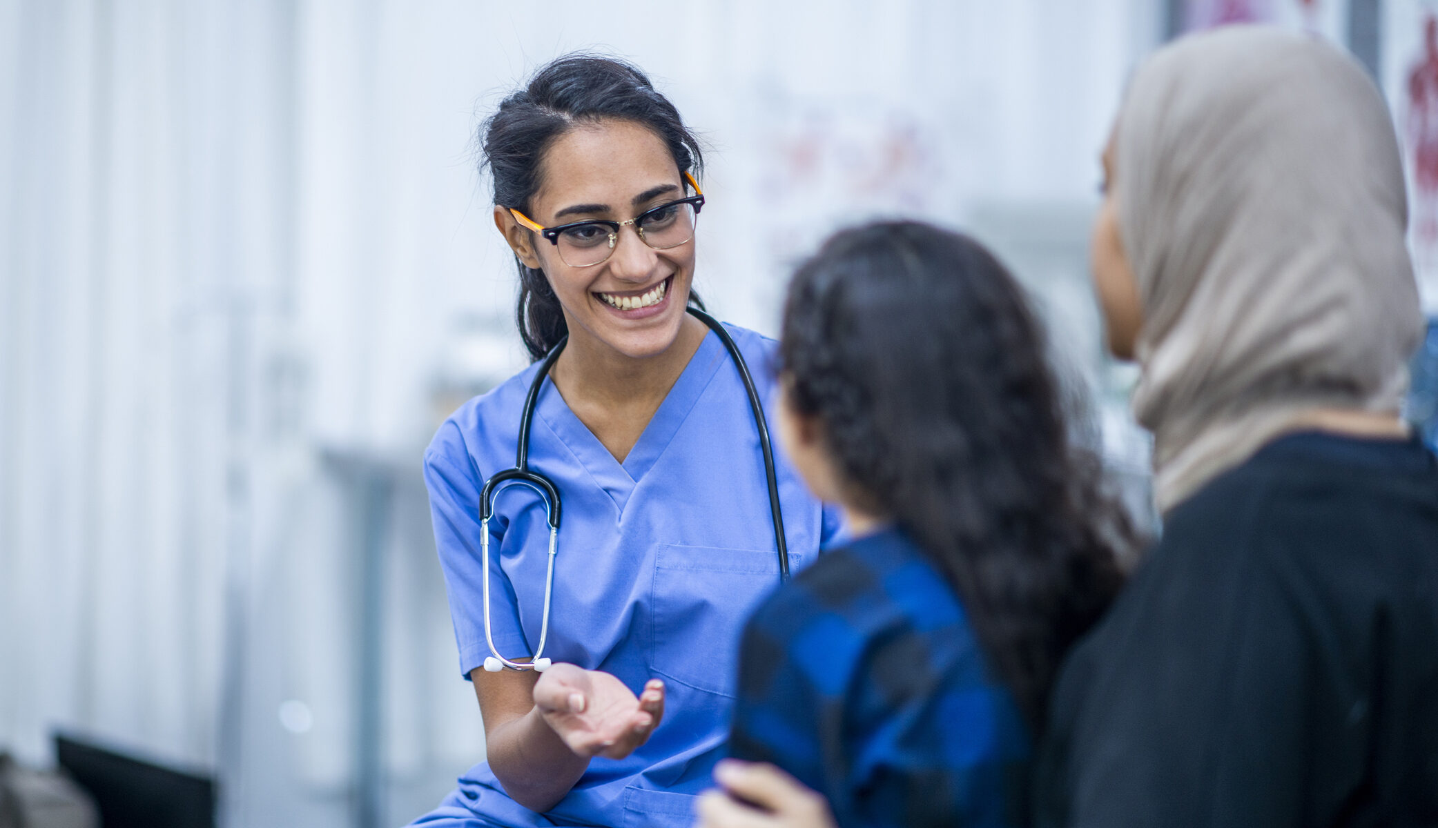 An Ethnic mother and daughter are indoors in a hospital. The daughter is about to have a checkup. Her mother and doctor are trying to comfort her.