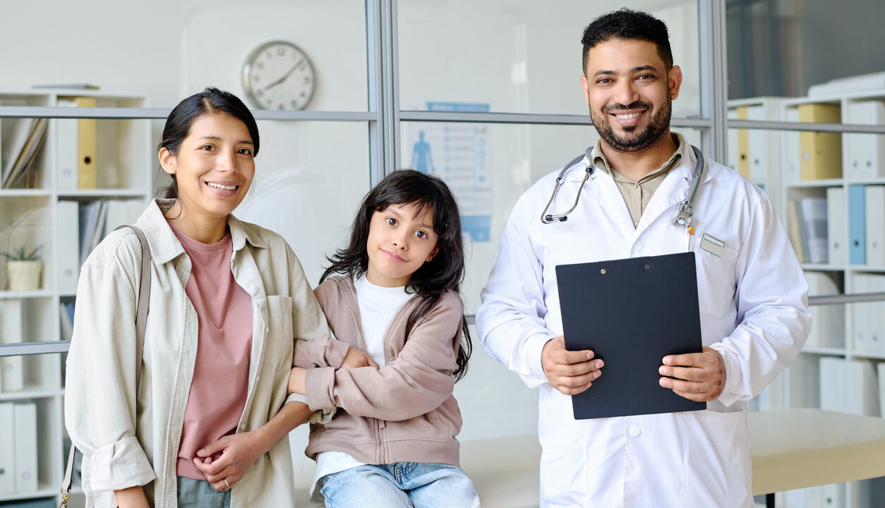 Portrait of mom with child smiling at camera together with pediatrician in office