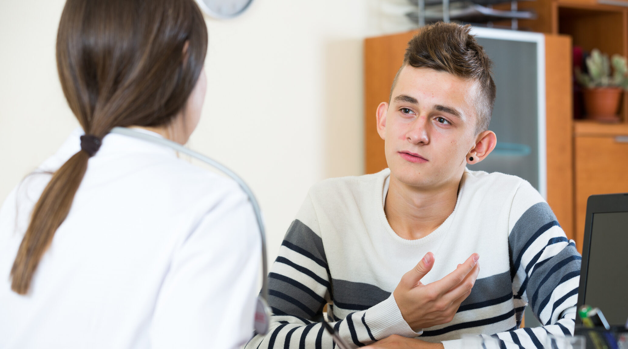 Professional physician consulting concerned teenage patient at clinic