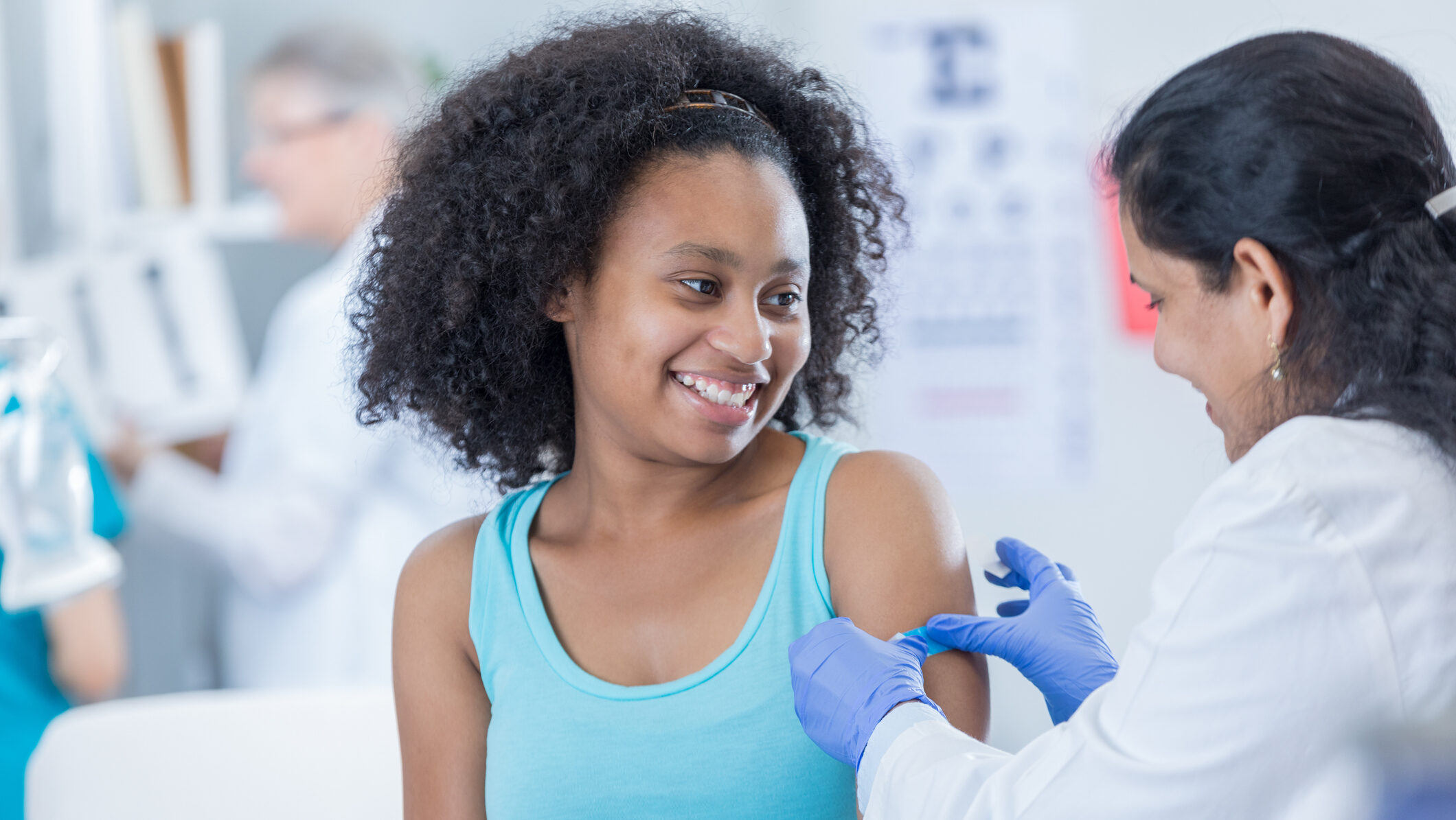 Female doctor puts a bandage on teenage girl's arm after receiving immunization.