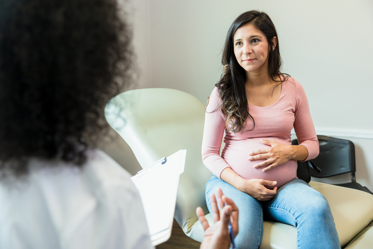 Expectant mother touches abdomen while listening to unrecognizable doctorExpectant mother touches abdomen while listening to unrecognizable doctor