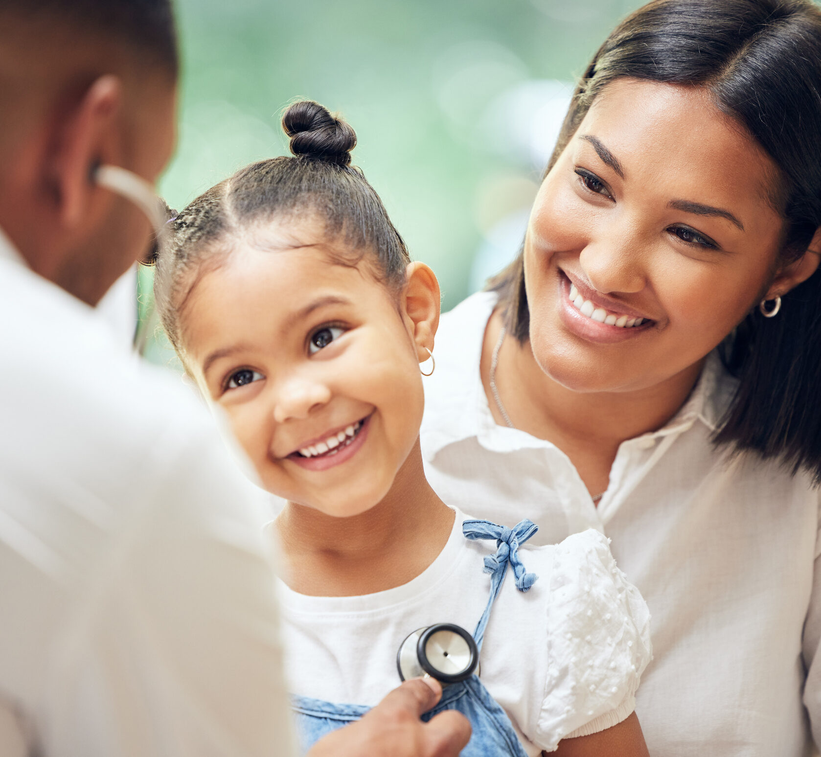 Male doctor examining happy little girl by stethoscope. Child sitting with mother while paediatrician listen to chest heartbeat. Mom holding daughter during trusted family doctor visit