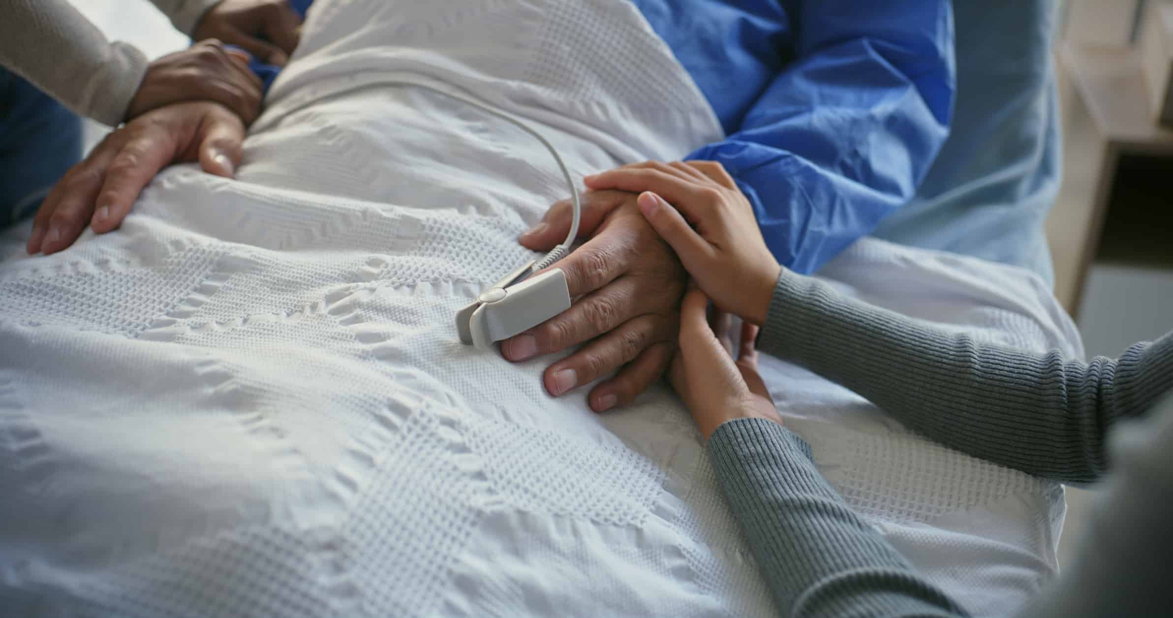 Family members holding hospice patient’s hand in hospital bed showing comfort, support, and compassionate end-of-life care