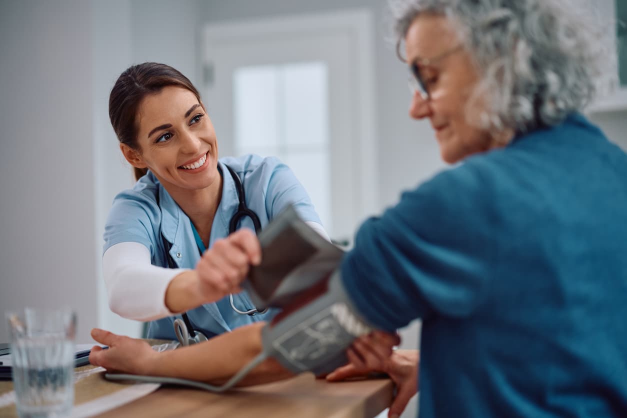 Female nurse measuring blood pressure of senior woman during home healthcare visit and wellness checkup