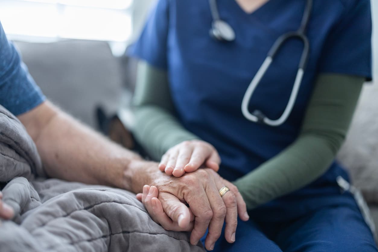 Hospice nurse holding senior patient’s hand at bedside, providing comfort, support, and compassionate in-home care