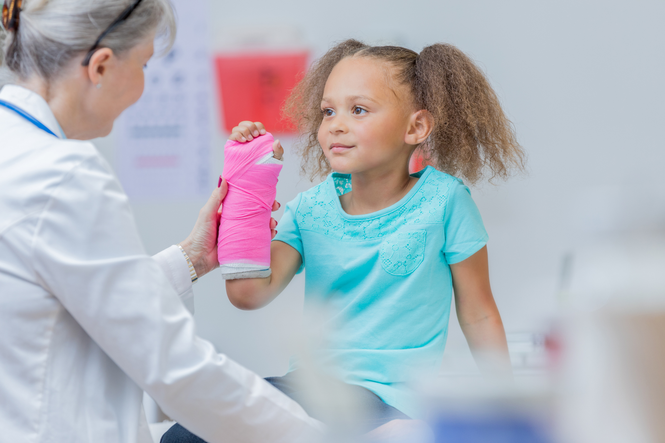 Doctor examines an elementary age mixed race girl's broken arm. The girl has a pink cast on her arm.