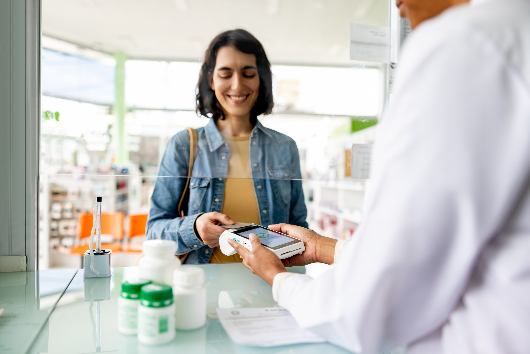 Happy Latin American woman paying by card while buying medicines at the pharmacy