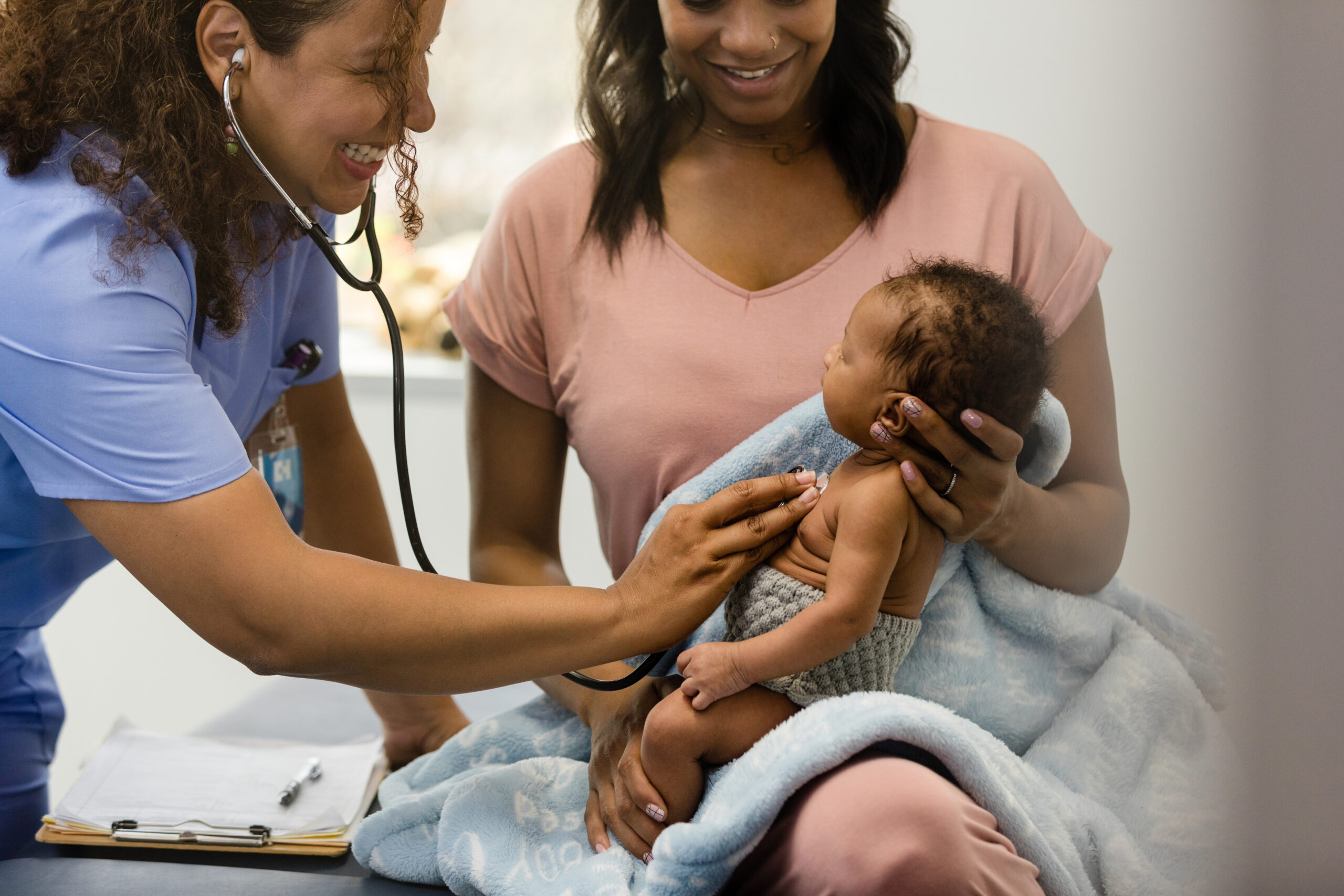 The smiling nurse practitioner uses her stethoscope to check the baby's heart and lungs.