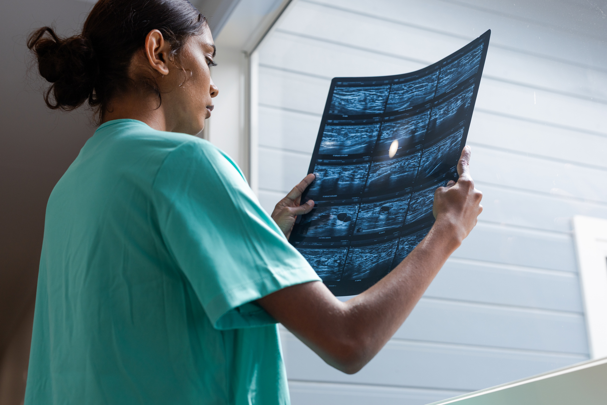 Young Aboriginal student doctor in medical scrubs reviews ultrasound scans by a large window in a medical clinic