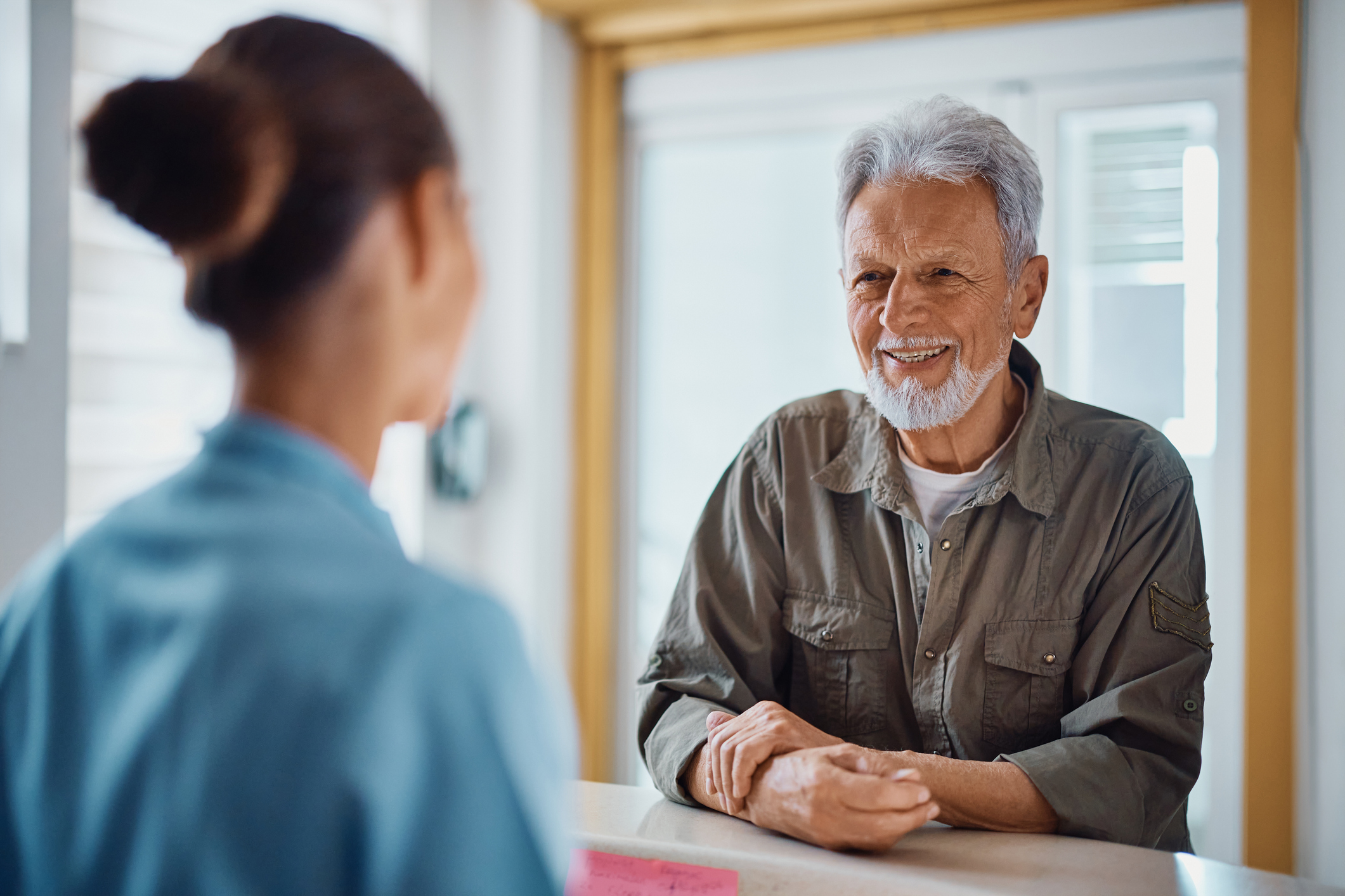 Happy mature man checking in doctor's office and communicating with a nurse at reception desk.