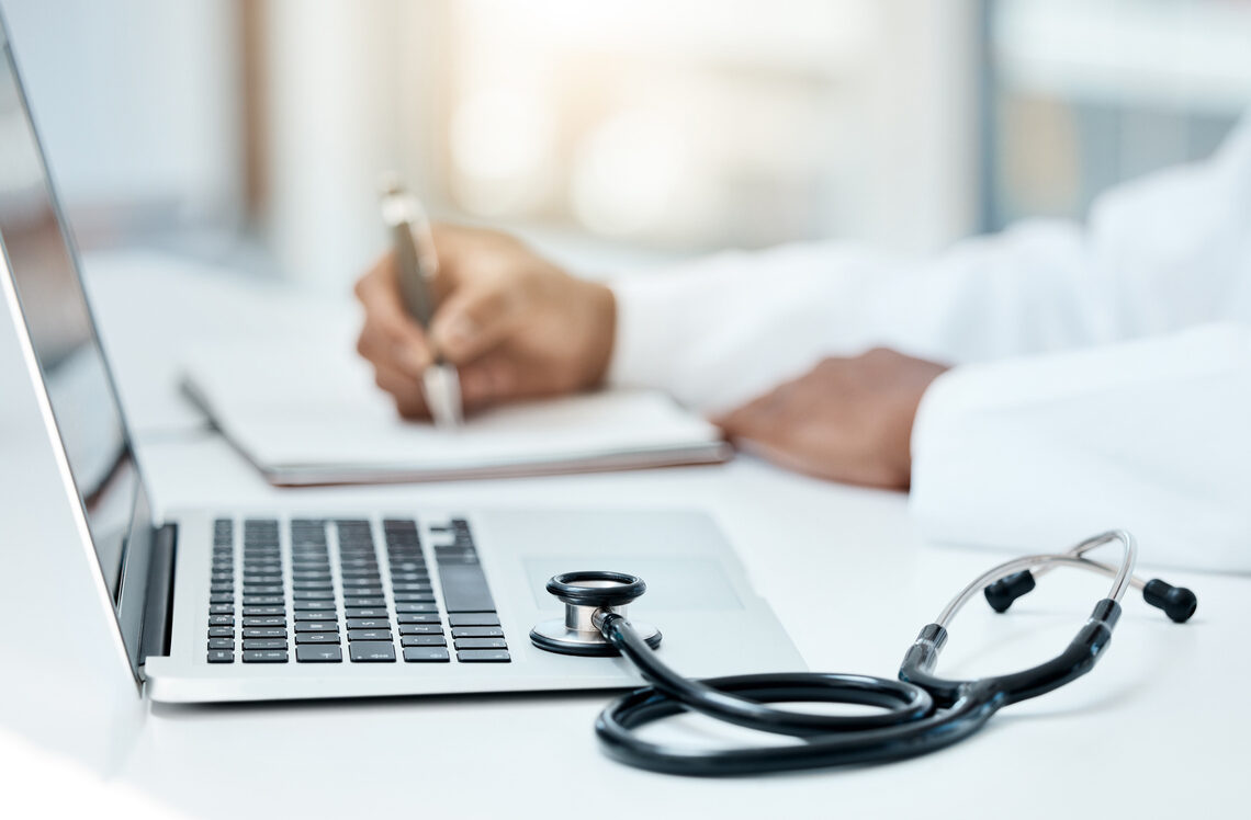 Laptop, stethoscope and doctor writing in notebook for research planning or medical tech innovation in hospital office. Healthcare medic worker, research strategy book notes and online communication