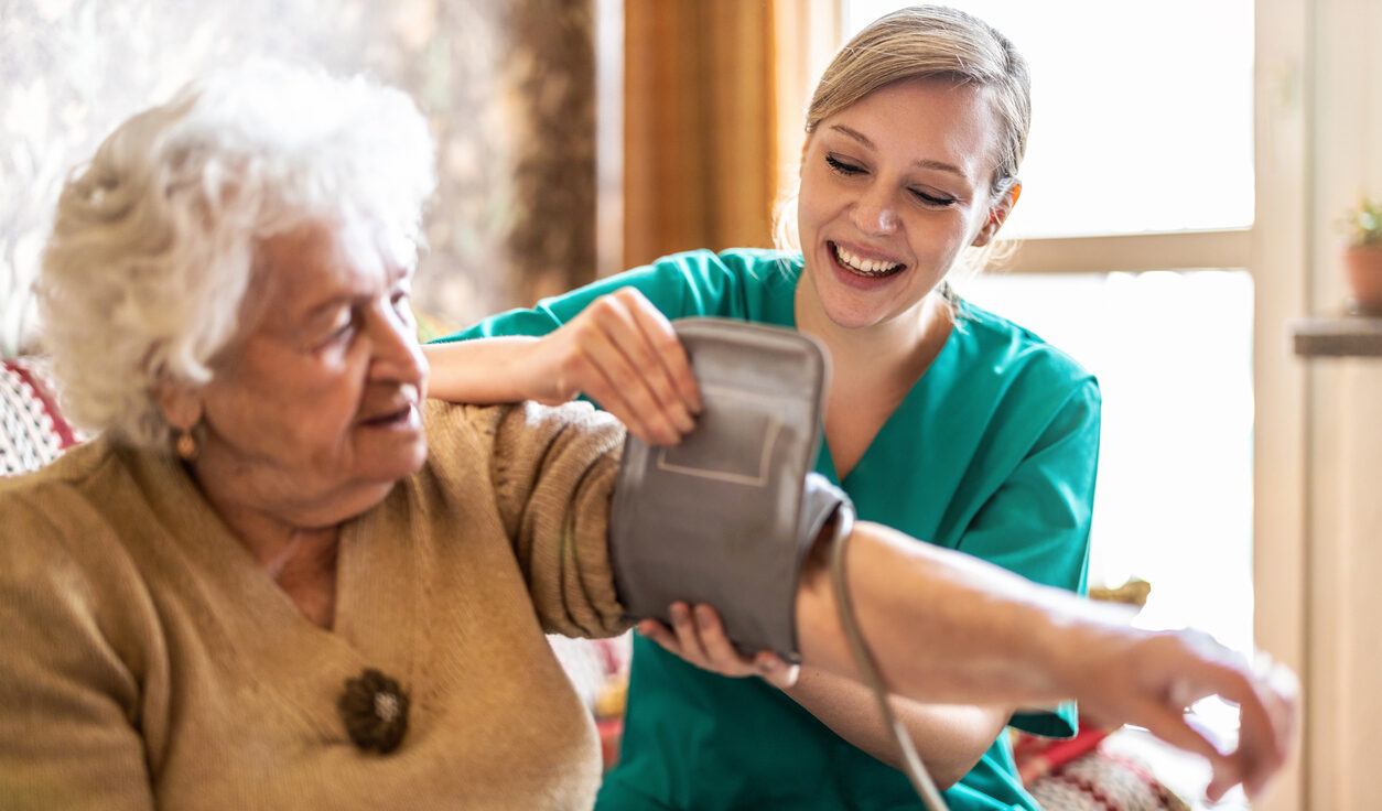 Female caretaker measuring senior woman's blood pressure at home