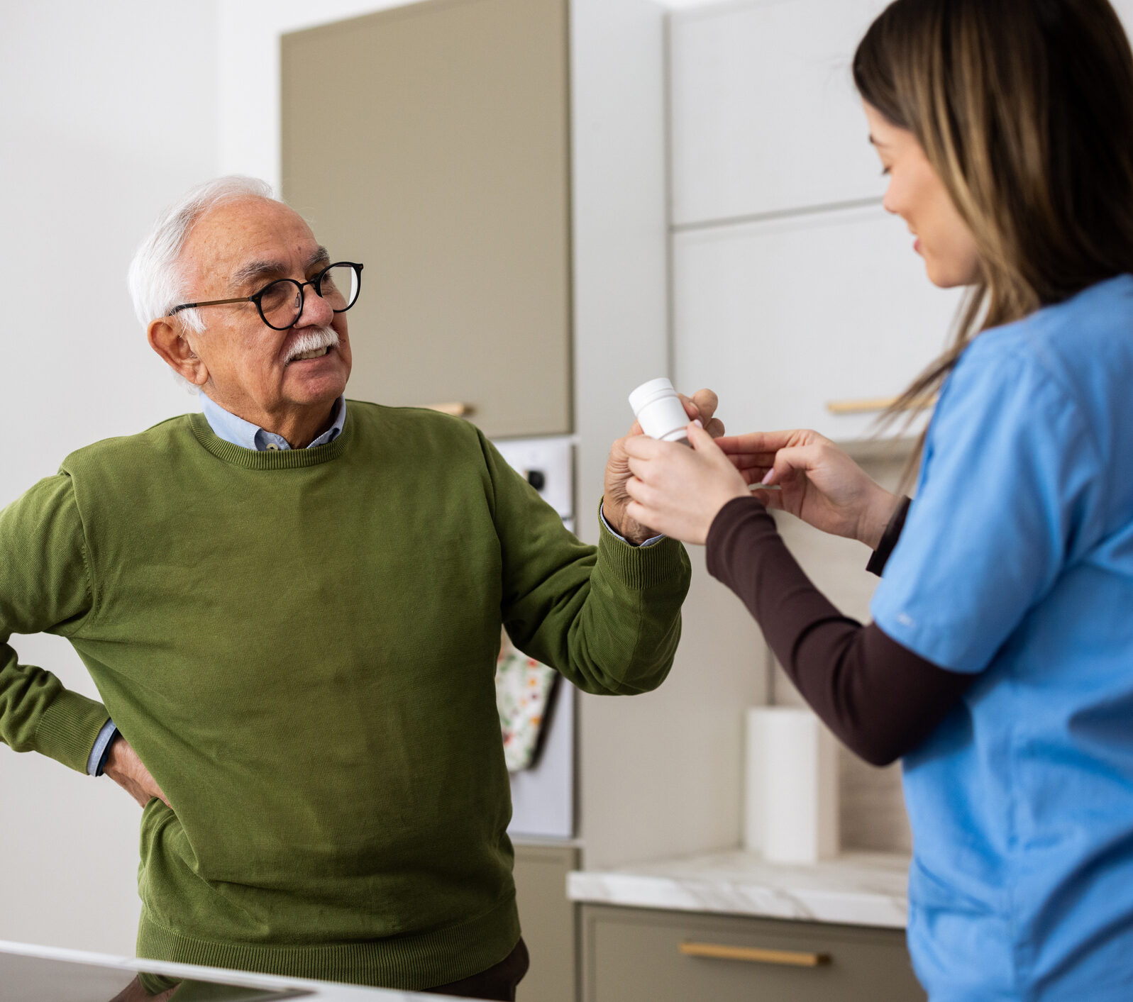 Caregiver giving medication to a senior man experiencing back pain at home
